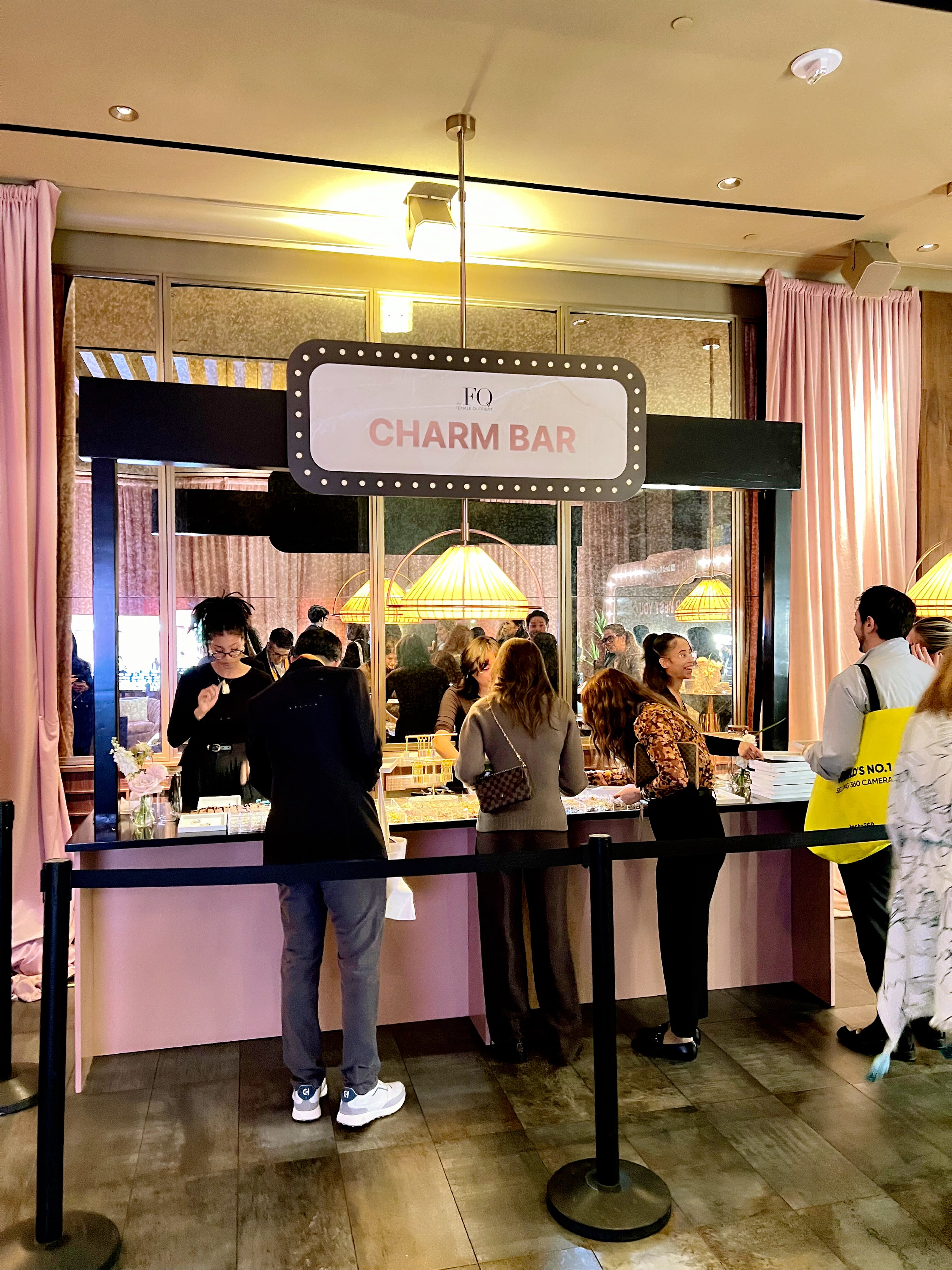 People waiting in line at a 'Charm Bar' inside a store with pink curtains.