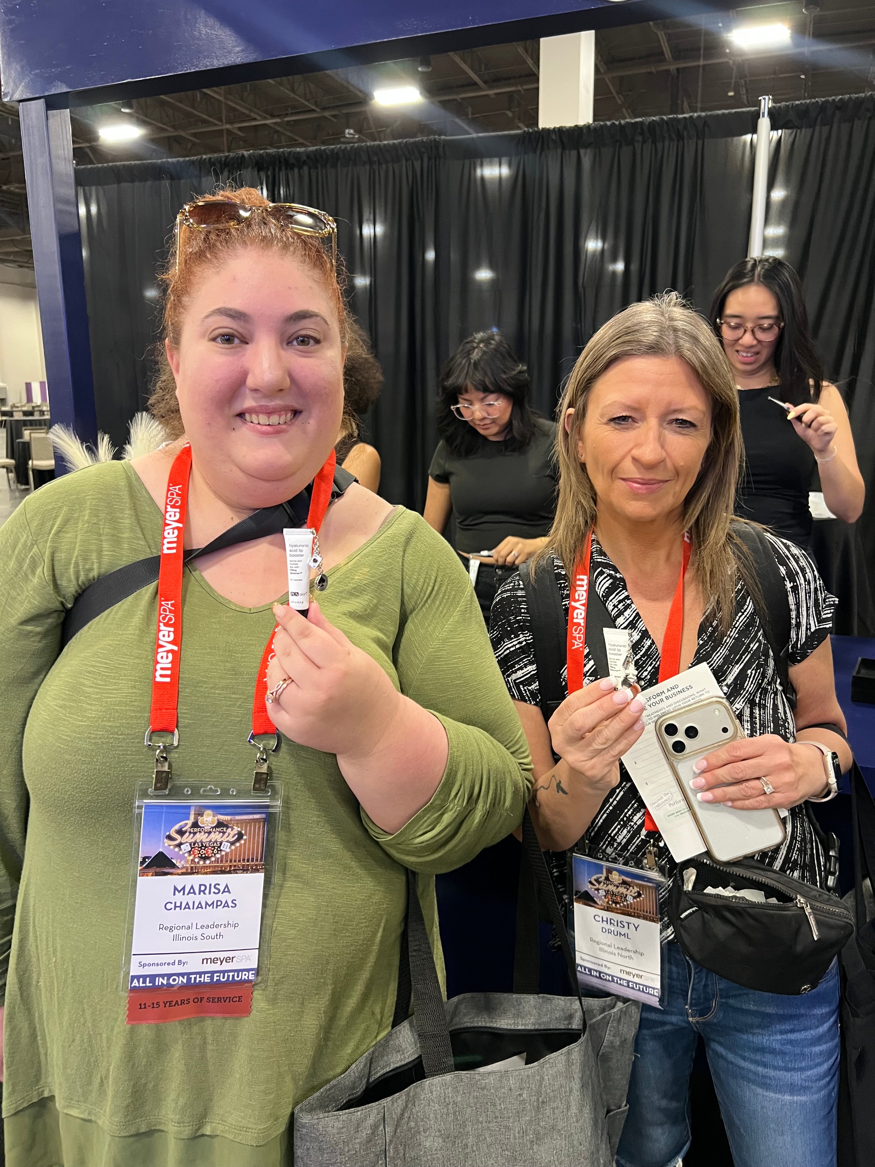 Event attendees displaying custom silver charms personalized at a Hey Beautiful interactive Lip Balm charm bar experience during a Spa conference.