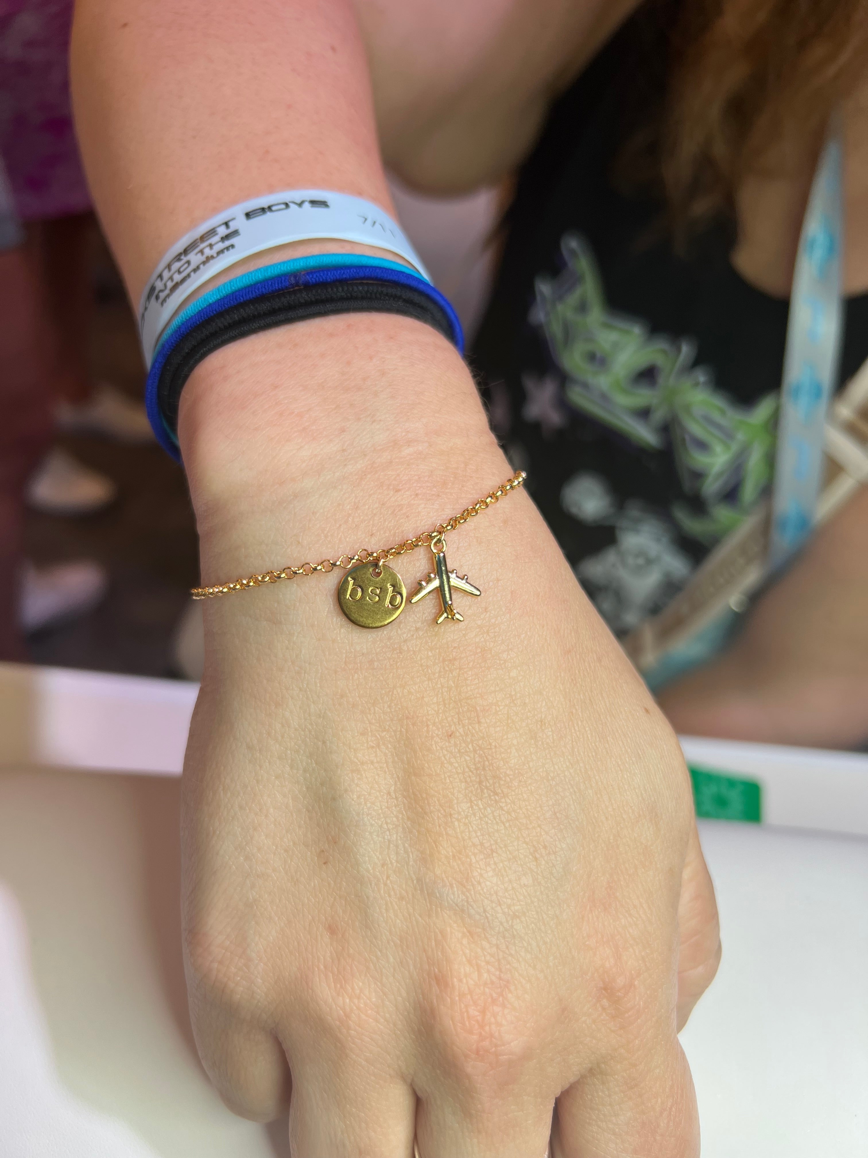 Close-up of a wrist with gold bracelet and a BSB and airplane charm