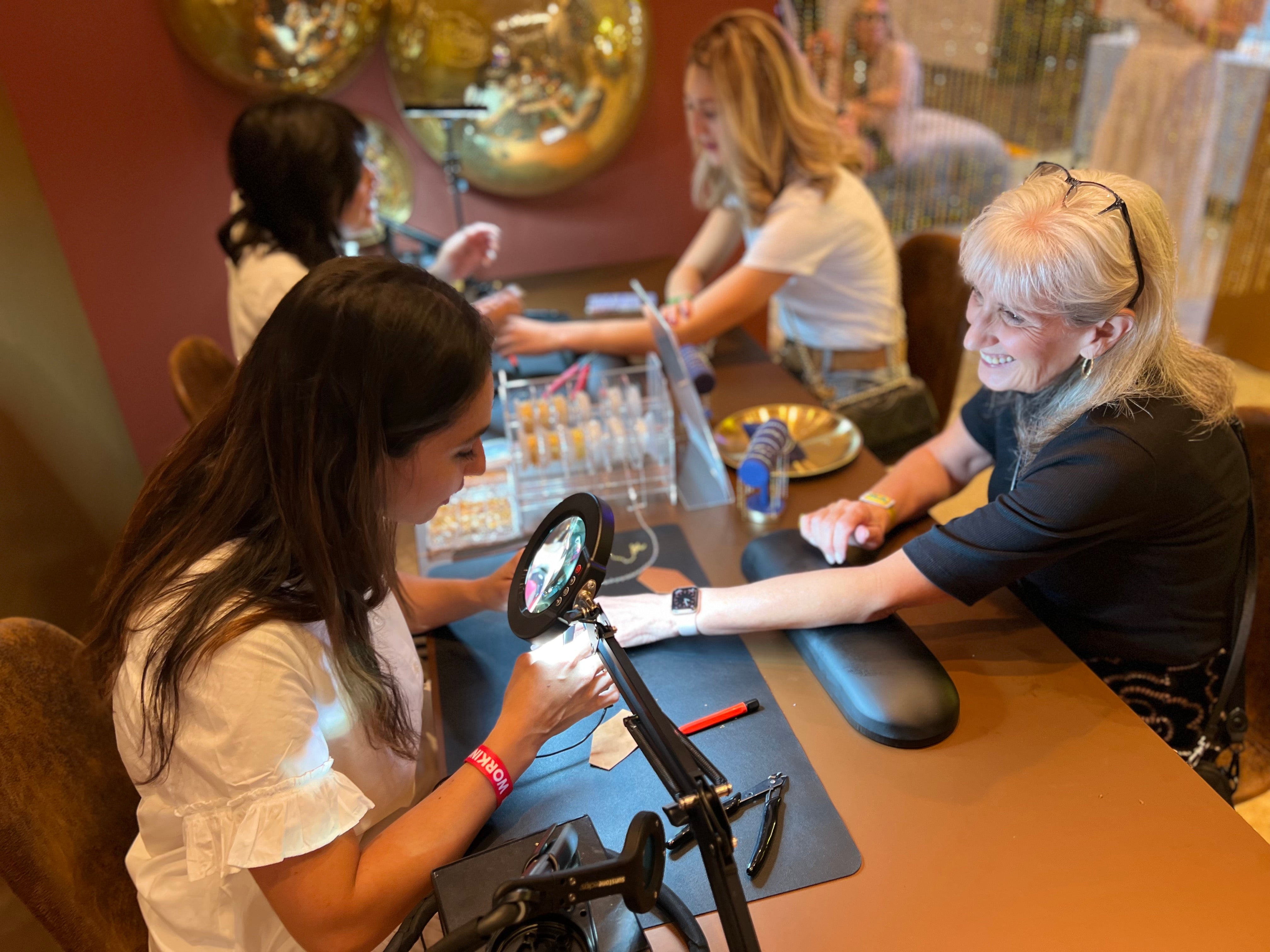 Two women at a permanent jewelry table smiling at a convention 